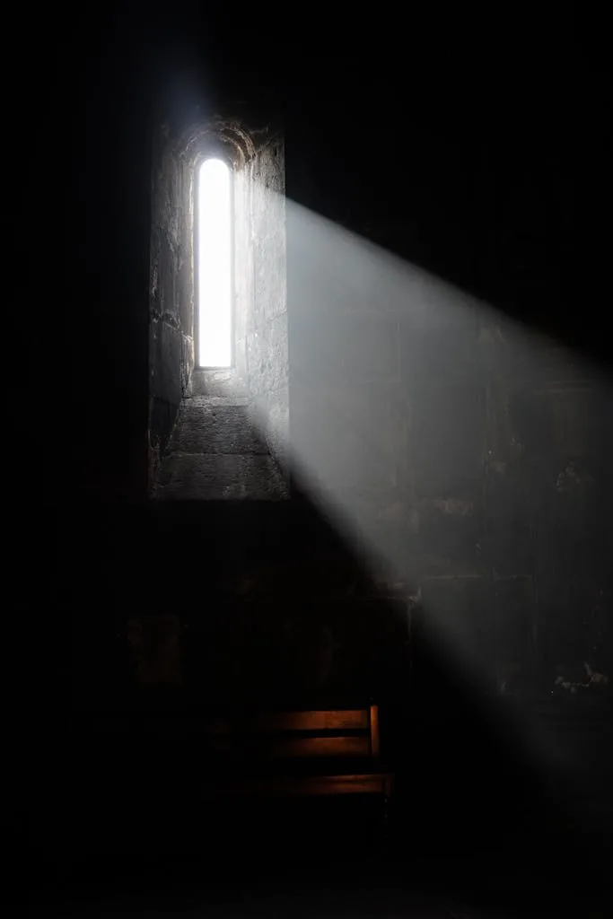 A dramatic beam of light streams through a narrow window, illuminating a dark room.