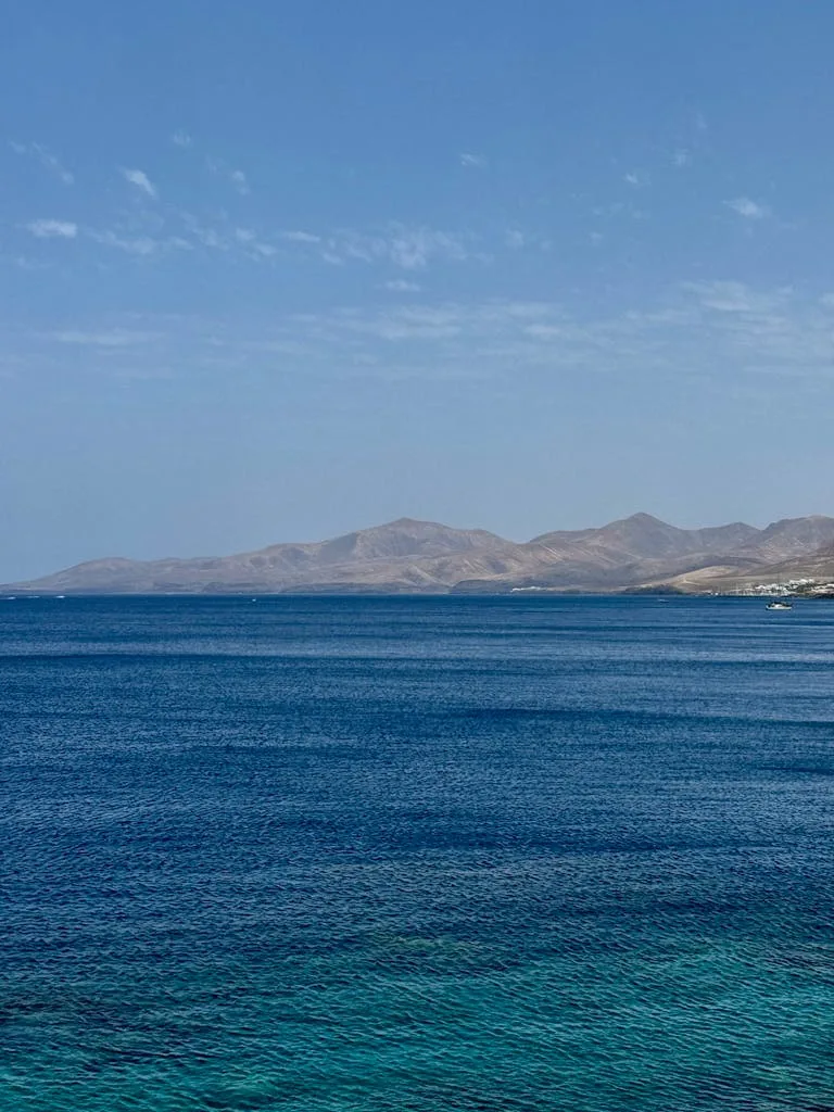 Beautiful view of Lanzarote coastline with clear blue ocean and distant mountains under a blue sky.